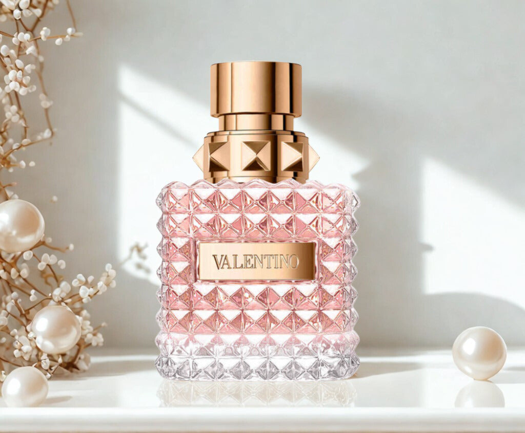 Pink perfume bottle with rose gold cap on a light background with natural light, bottle surrounded by white pearls